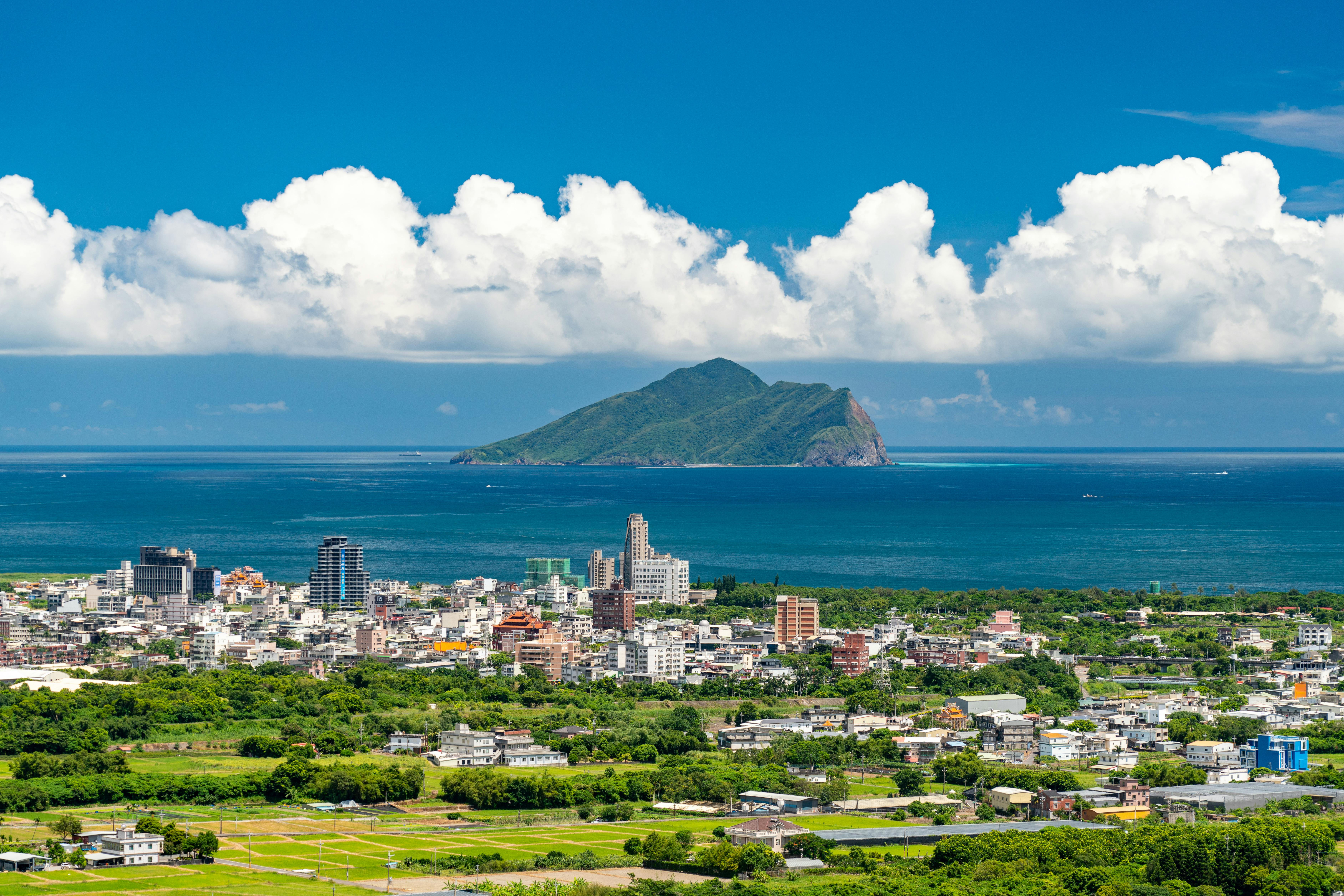 pexels-photo-9363391-9363391 Aerial view of a vibrant Taiwanese cityscape with lush greenery and a striking island in the background.